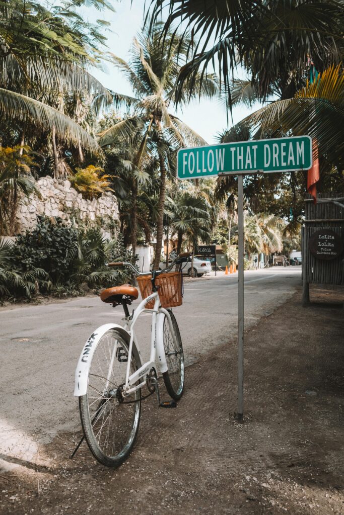 pexels-photo-3727253-3727253 A bicycle near an inspirational sign 'Follow That Dream' in Tulum, Mexico with palm trees around.